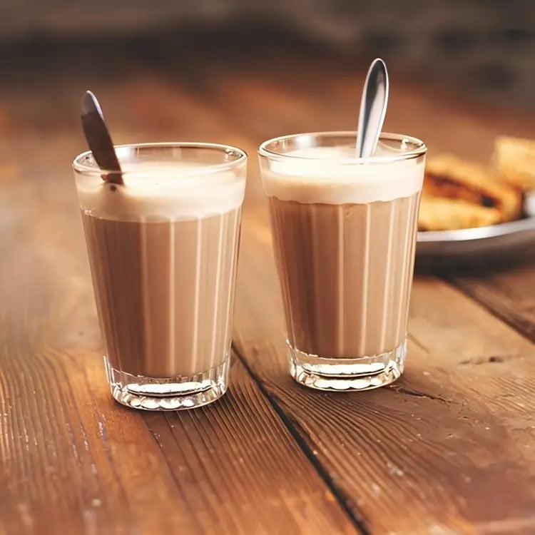 Dwie szklanki chai latte ze spienionym mlekiem na drewnianym stole, idealne na rozgrzewający moment z herbatą korzenną.