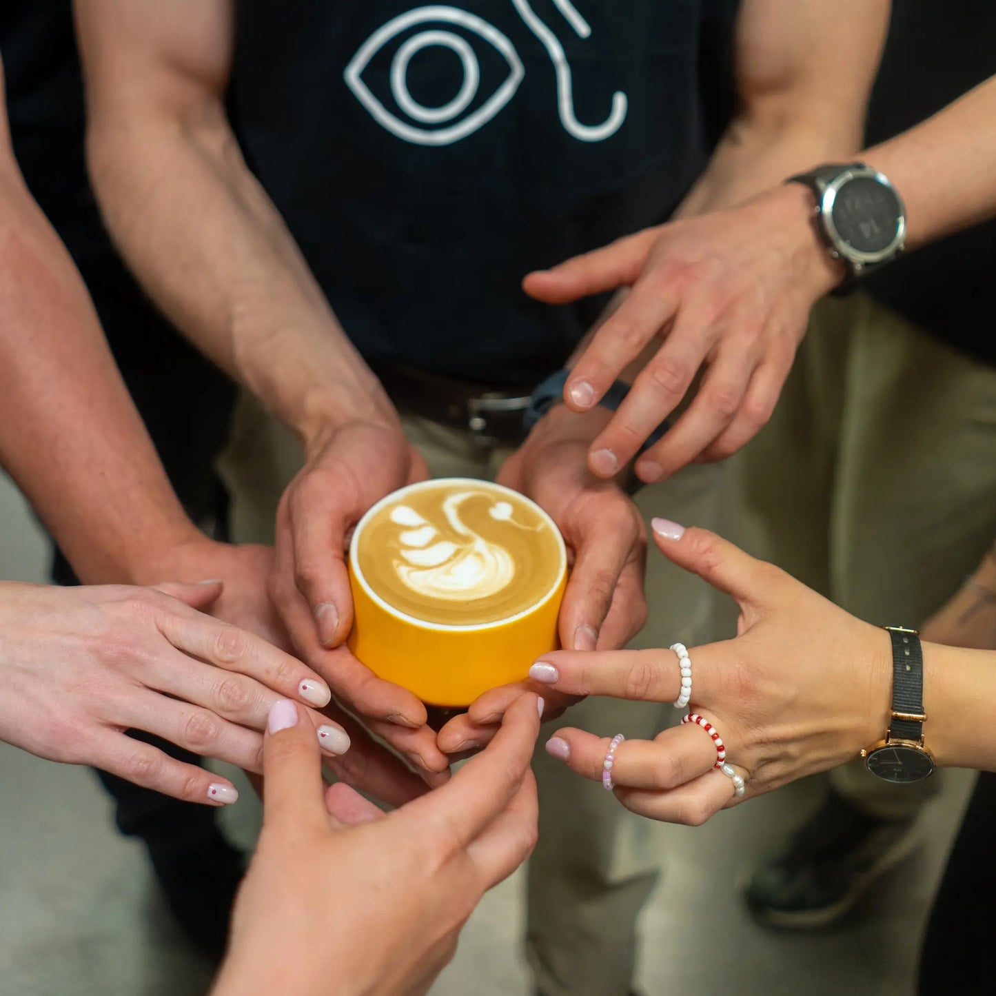 Grupa osób trzymająca filiżankę kawy z latte art w żółtej filiżance – symbol wspólnoty i pasji do kawy w JAVA Coffee Roasters.