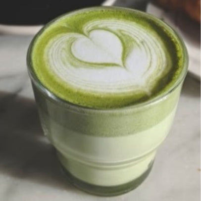 Szklanka matcha latte z pięknym wzorem serca wykonanym w technice latte art, ustawiona na stole.