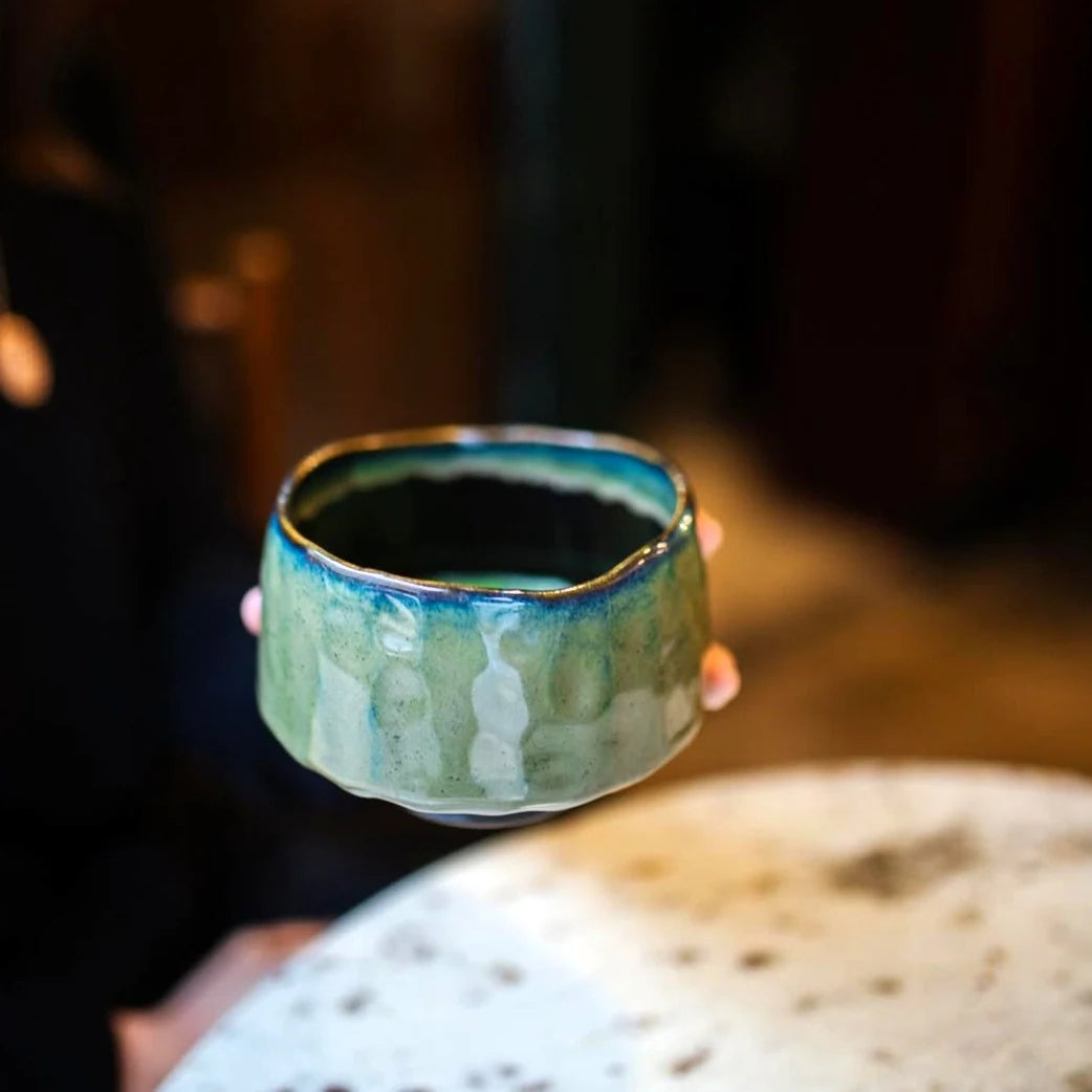 Matchawan Gyoku – zielona, szkliwiona czarka do matchy trzymana w dłoniach, ręcznie wykonana ceramika w klimatycznym, ciepłym wnętrzu.