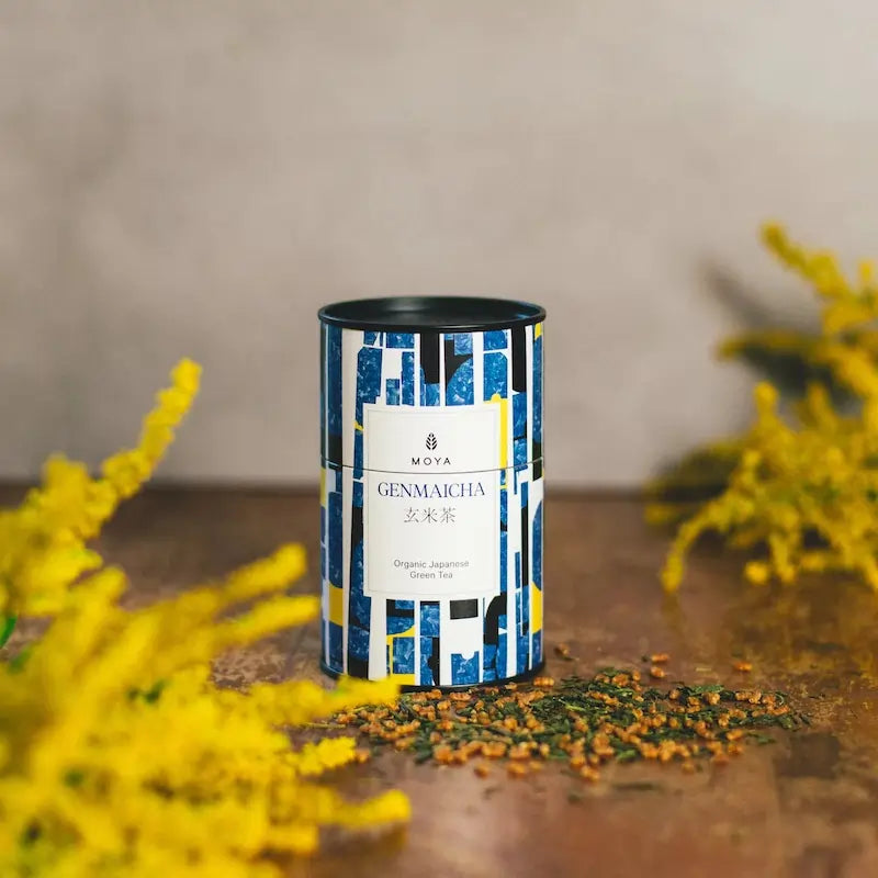 Herbata Moya Genmaicha – organiczna japońska zielona herbata liściasta w ozdobnej puszce, na tle żółtych kwiatów