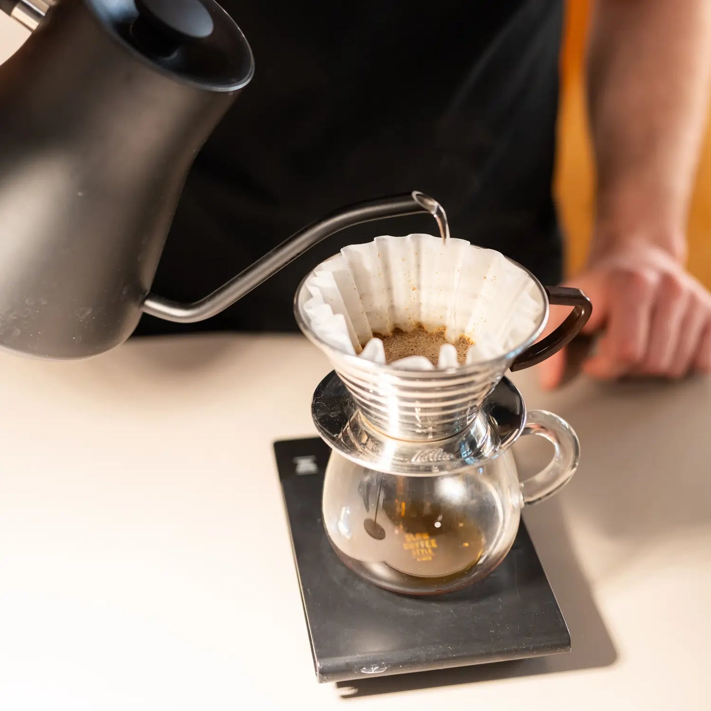 Parzenie kawy metodą V60 – barista zalewa filtr wodą, kawa spływa do dzbanka na wadze.