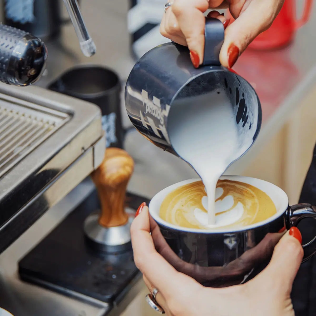 Spienianie napoju Sproud i tworzenie latte art w filiżance kawy przez baristkę przy ekspresie.