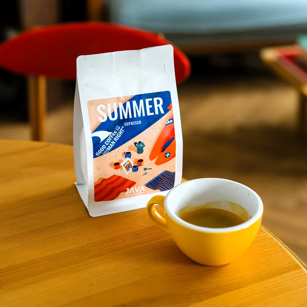 Paczka Summer Espresso od JAVA Coffee Roasters ustawiona obok filiżanki espresso na drewnianym stoliku w przytulnym wnętrzu