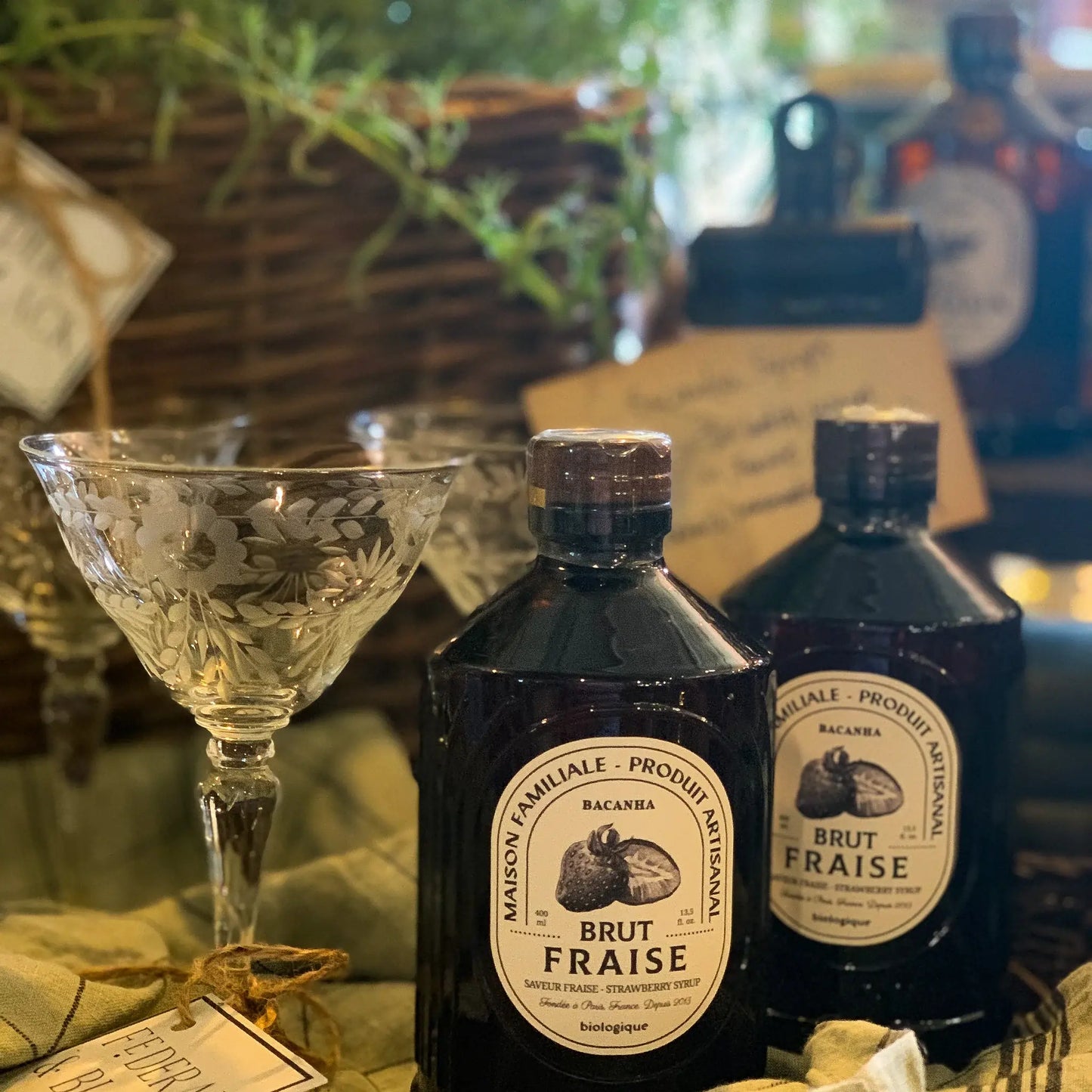 Syrop Bacanha o smaku truskawkowym – butelki syropu ustawione obok kieliszków koktajlowych w rustykalnej aranżacji