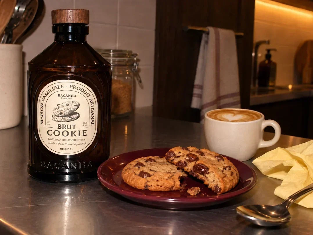 Butelka syropu Bacanha Cookie obok ciasteczek czekoladowych i filiżanki latte na blacie kuchennym