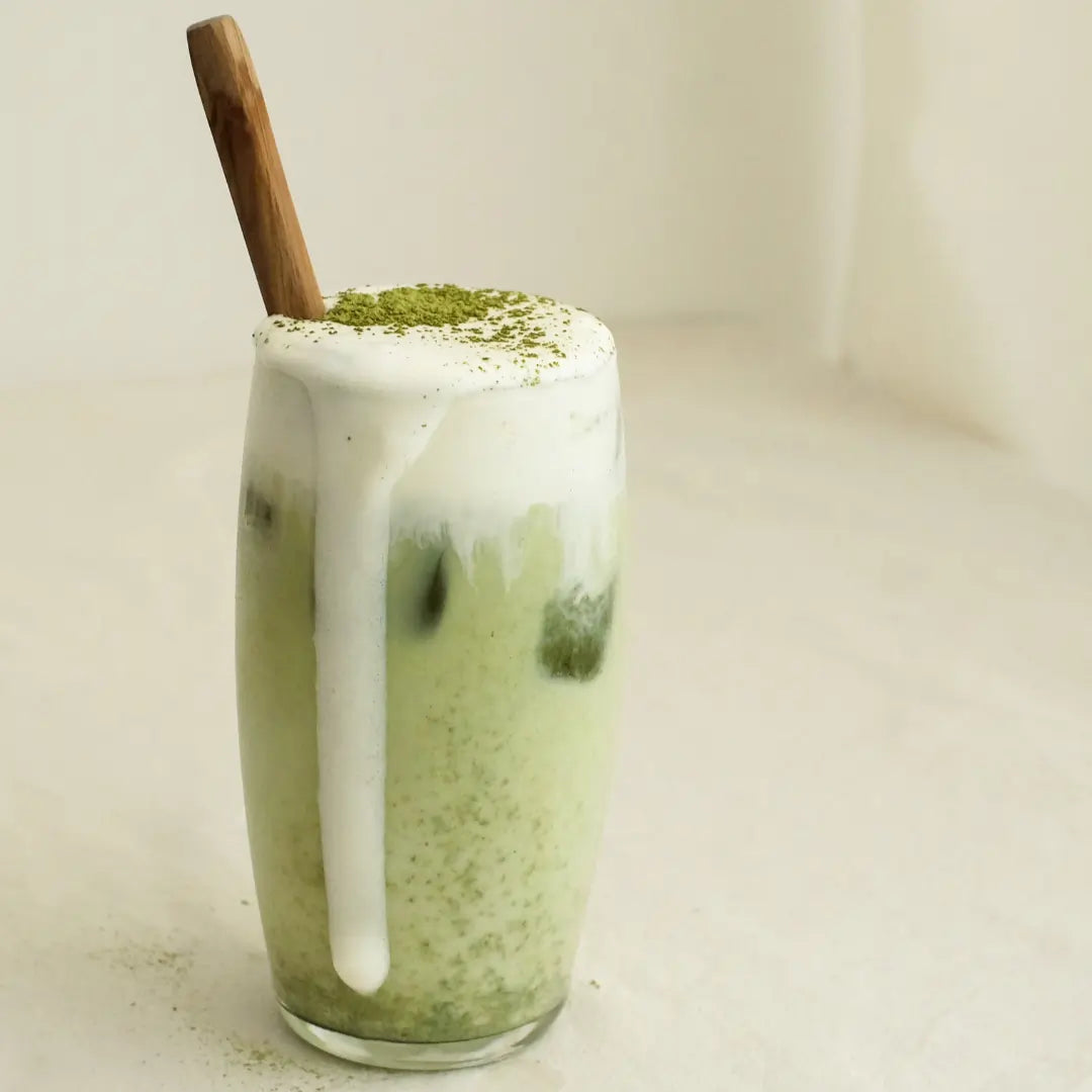Szklanka matcha latte na mleku kokosowym z gęstą mleczną pianką i posypką z proszku matcha