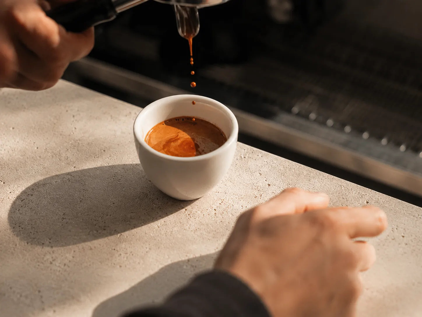 Espresso lungo nalewane z ekspresu do białej filiżanki, dłonie baristy widoczne przy blacie