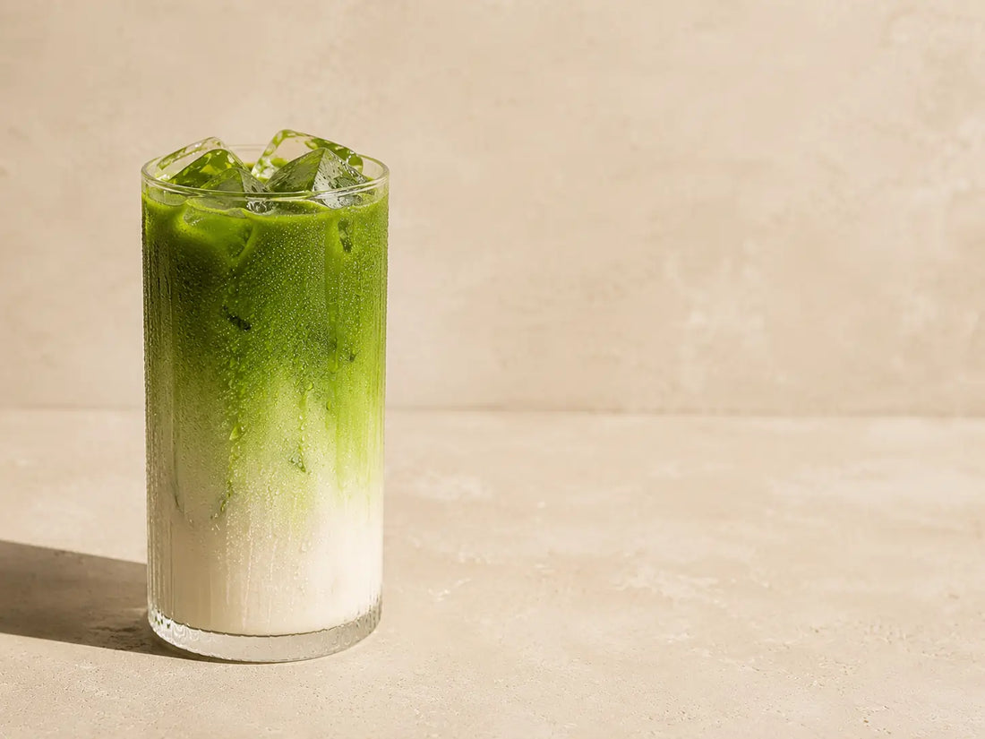 Iced matcha latte w szklance z widocznym dwuwarstwowym, zielono-mlecznym rozdzieleniem, podane na jasnym tle