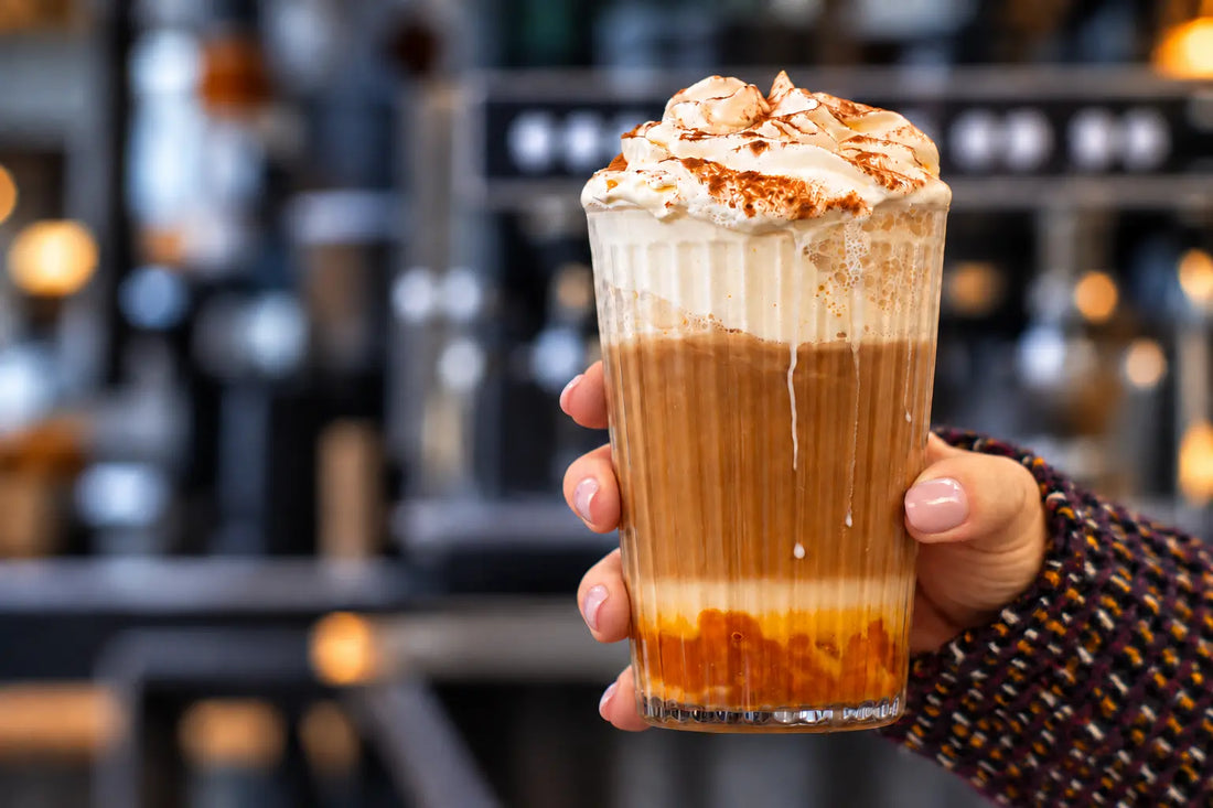 Pumpkin Spice Latte with whipped cream and cinnamon in a tall glass held in a hand