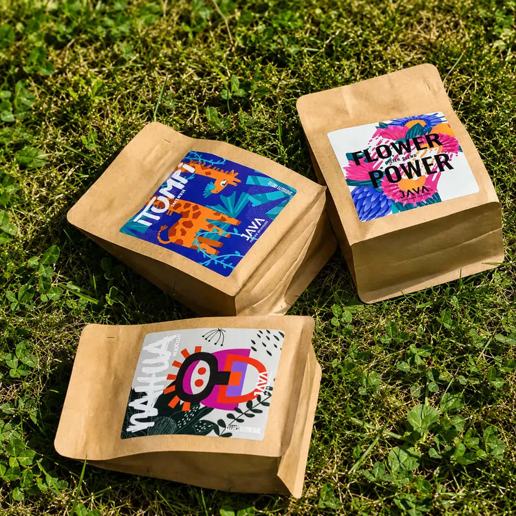 Kawy specialty JAVA Coffee Roasters – Flower Power, Nahua Mexico i Tanzania Itumpi ułożone na zielonej trawie podczas plenerowej sesji zdjęciowej .