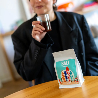 Kawa specialty Bali Kintamani od JAVA Coffee na pierwszym planie, w tle degustacja świeżo palonej kawy w nowoczesnym wnętrzu w Warszawie
