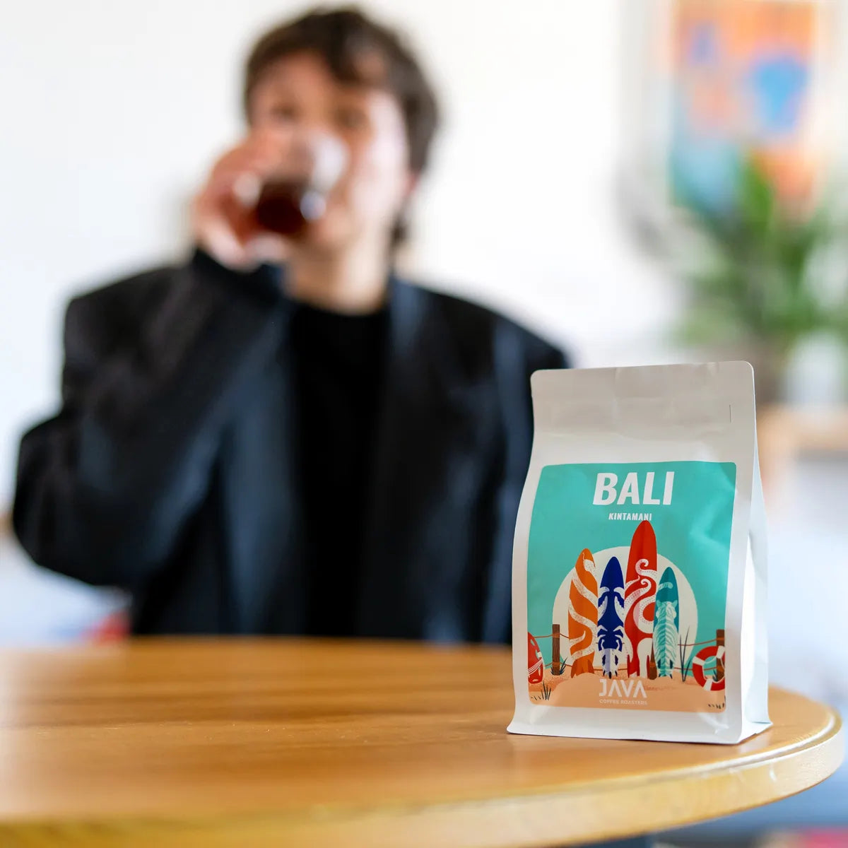 Kawa specialty Bali Kintamani od JAVA Coffee na pierwszym planie, w tle degustacja świeżo palonej kawy w nowoczesnym wnętrzu w Warszawie