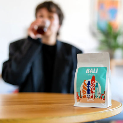 Kawa specialty Bali Kintamani od JAVA Coffee na pierwszym planie, w tle degustacja świeżo palonej kawy w nowoczesnym wnętrzu w Warszawie