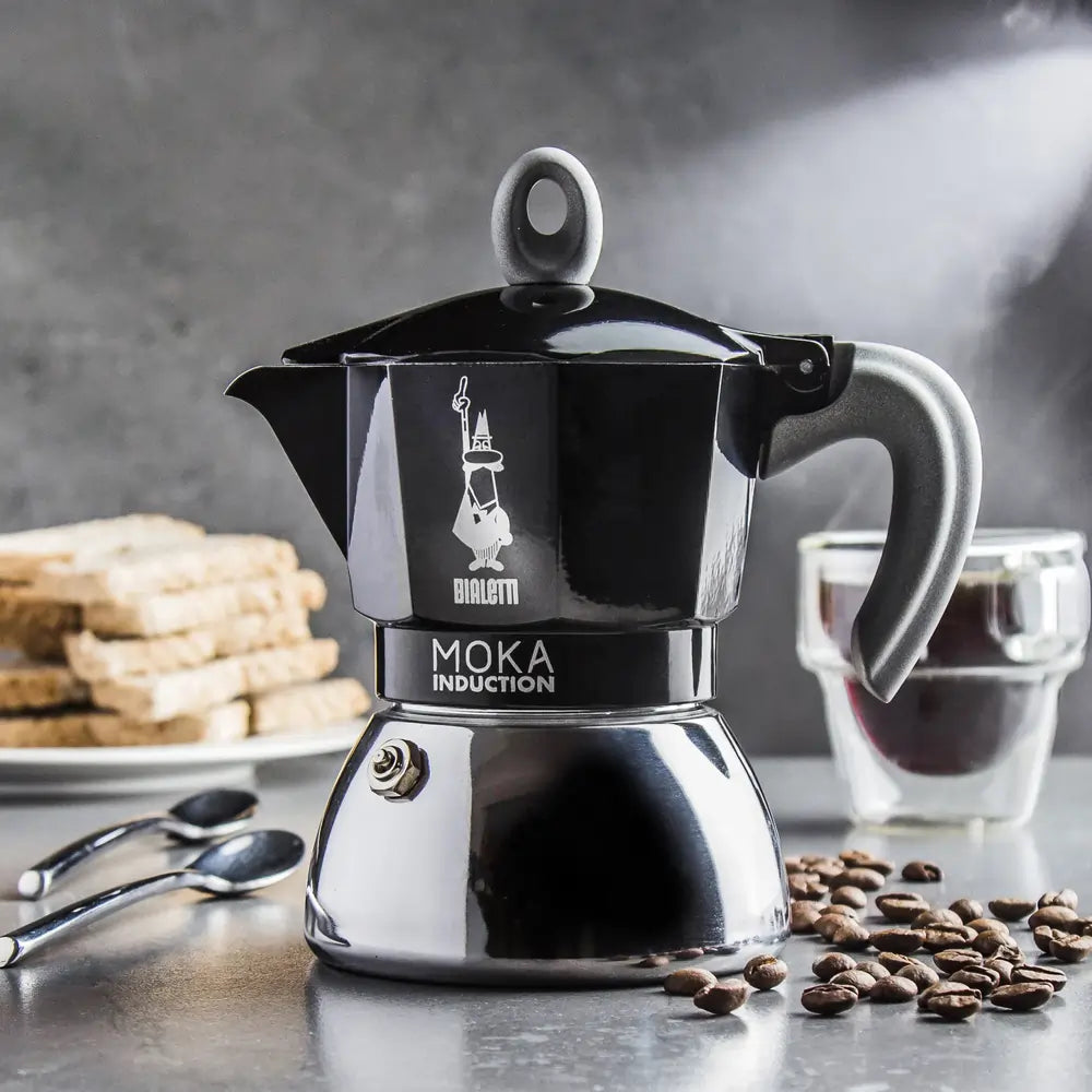 Kawiarka Bialetti Moka Induction 4TZ czarna w kuchni, kawiarka do kawy na indukcję, ziarna kawy i filiżanka espresso, zdjęcie lifestyle