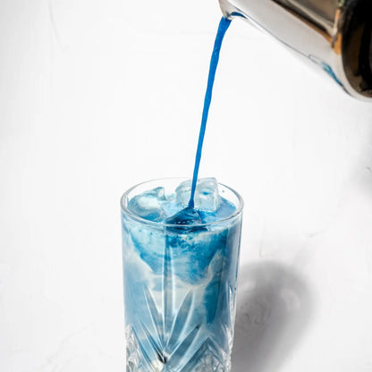 Niebieskie iced latte ze spiruliną nalewane do szklanki z kostkami lodu na jasnym tle