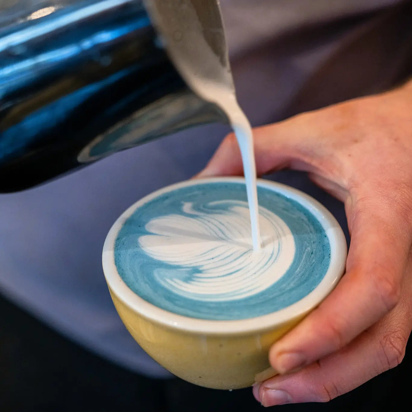 Niebieskie latte ze spiruliną z latte art przygotowywane przez baristę w ceramicznej filiżance