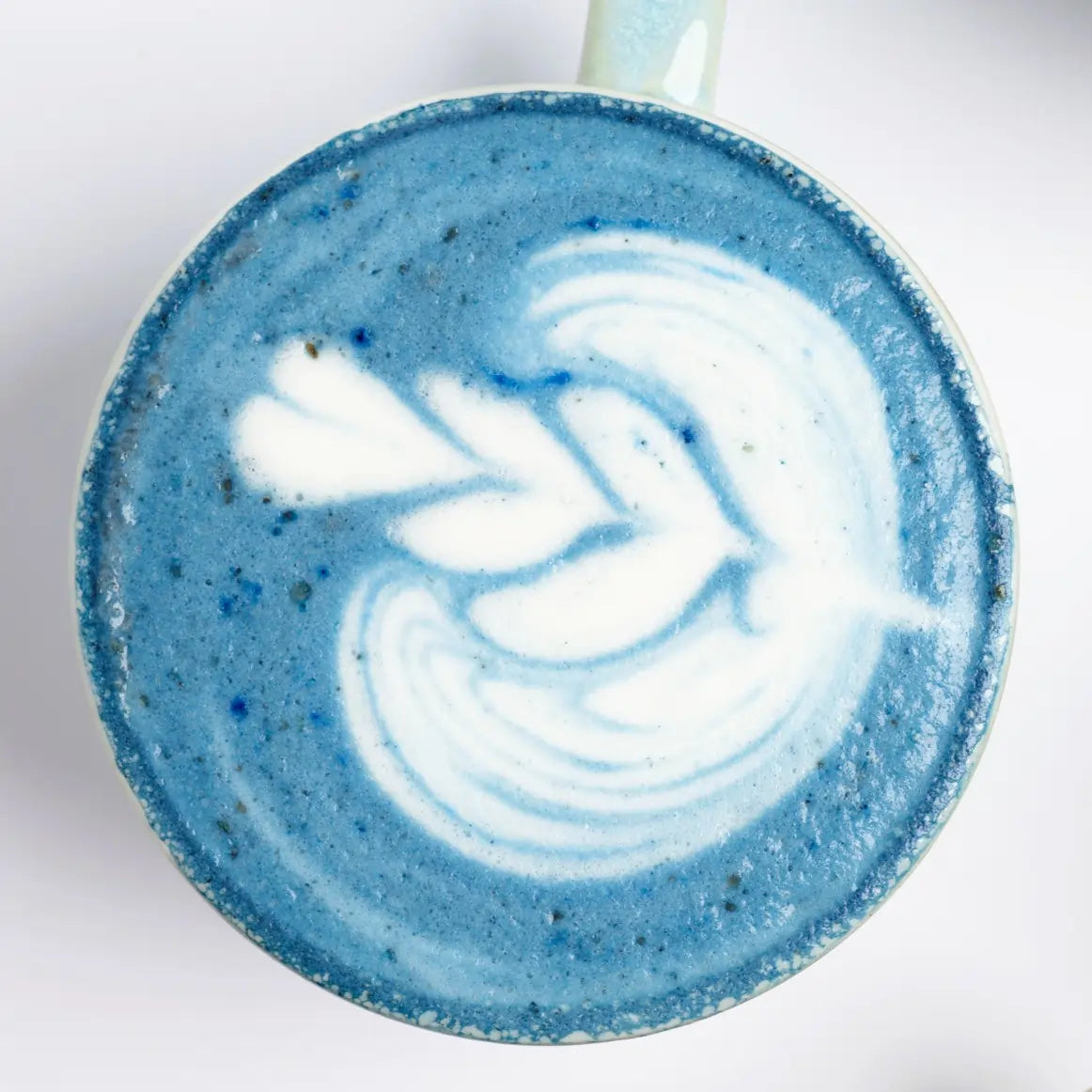 Zbliżenie na niebieskie latte ze spiruliną z białym latte art widziane z góry