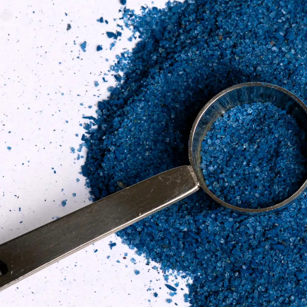 Niebieski proszek do latte ze spiruliną w metalowej miarce na jasnym tle z rozsypanym produktem
