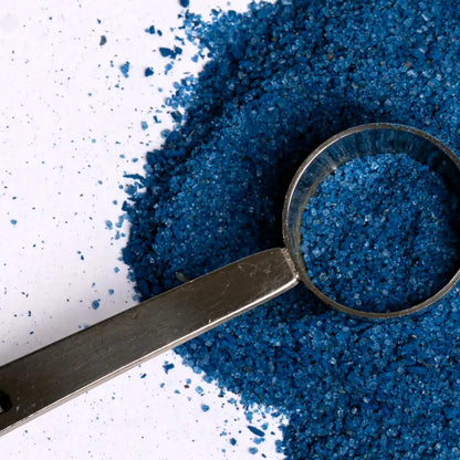 Niebieski proszek do latte ze spiruliną w metalowej miarce na jasnym tle z rozsypanym produktem