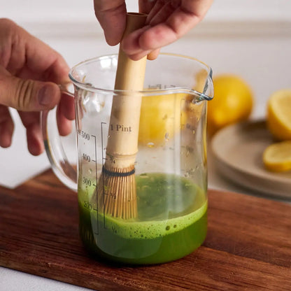 Przygotowanie matchy chasenem – bambusowa miotełka do matchy spienia zieloną herbatę matcha w szklanym dzbanku, proces przygotowania matcha latte