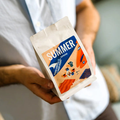 Burundi Ninga Summer Espresso JAVA Coffee Roasters trzymana w dłoni obok filiżanki świeżo zaparzonego espresso