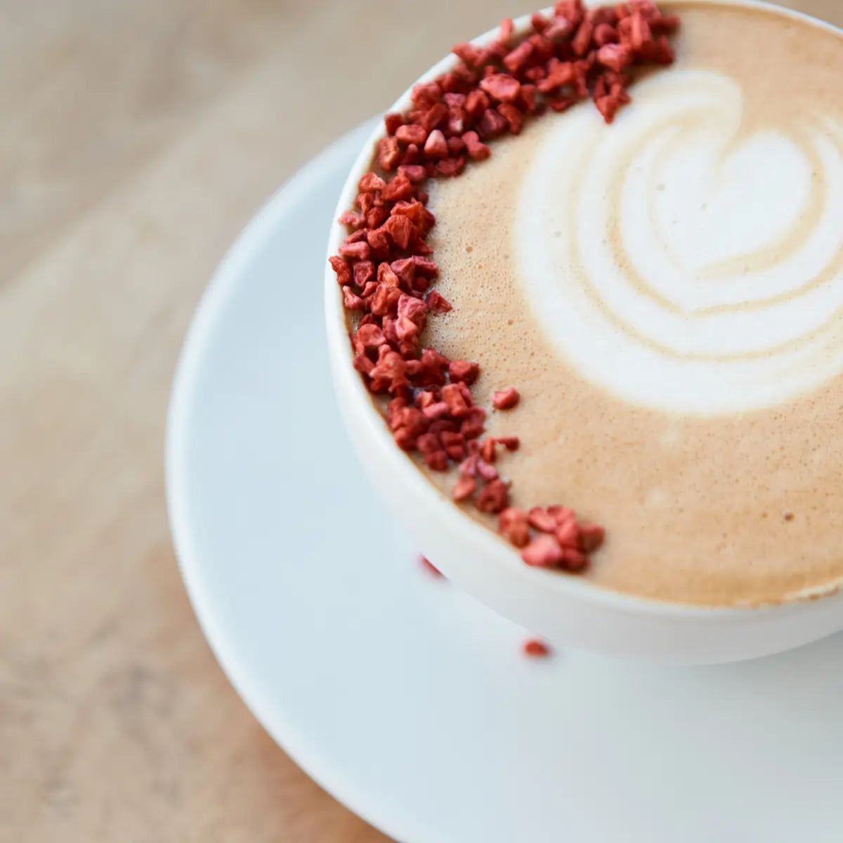 Zbliżenie na filiżankę cappuccino ozdobioną suszonymi malinami na mlecznej piance. Delikatny wzór serca w latte art.