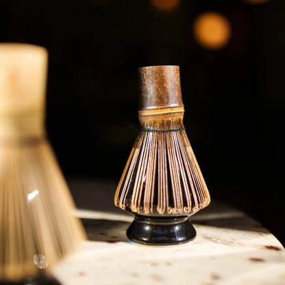 Bambusowa miotełka do matchy chasen na czarnym ceramicznym stojaku kusenaoshi w ciepłym, klimatycznym świetle