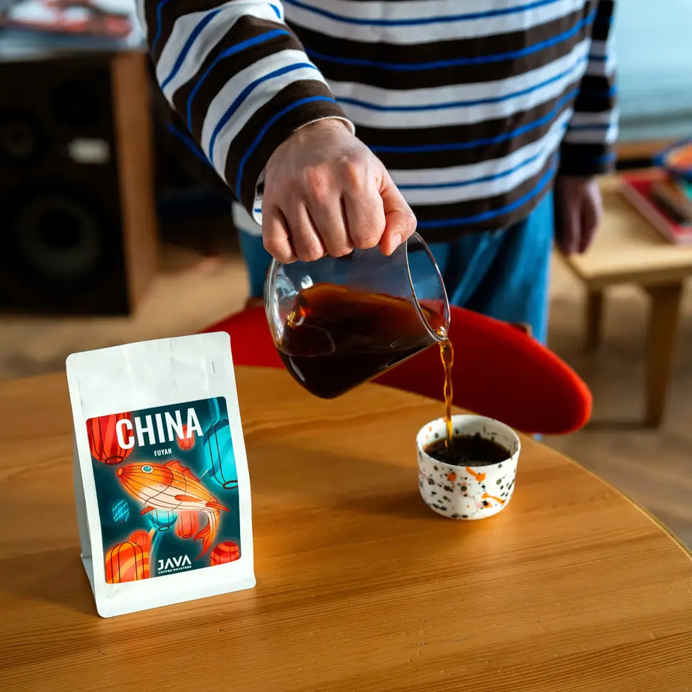 Parzenie kawy specialty China Fuyan od JAVA Coffee Roasters – nalewanie kawy przelewowej ze szklanego dzbanka do filiżanki, opakowanie kawy na drewnianym stole