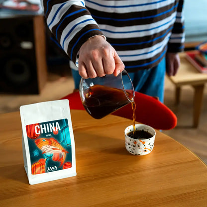 Parzenie kawy specialty China Fuyan od JAVA Coffee Roasters – nalewanie kawy przelewowej ze szklanego dzbanka do filiżanki, opakowanie kawy na drewnianym stole