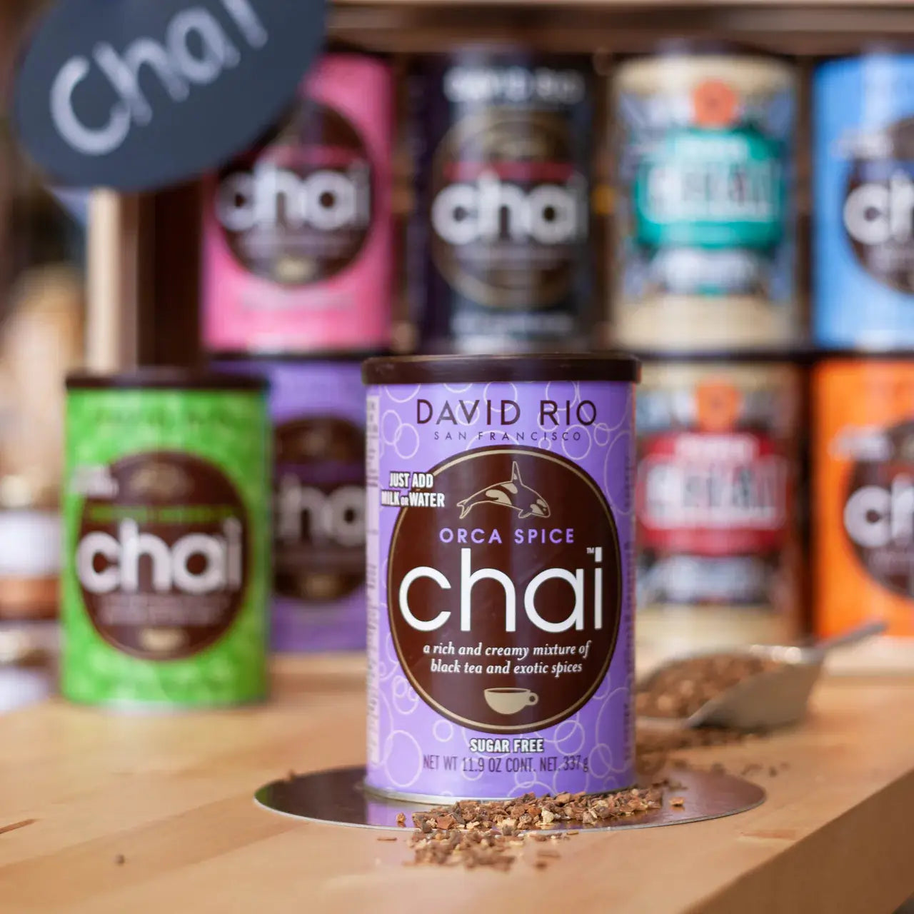 Puszka David Rio Orca Spice Chai – herbata chai latte bez cukru, na tle kolorowych opakowań innych smaków