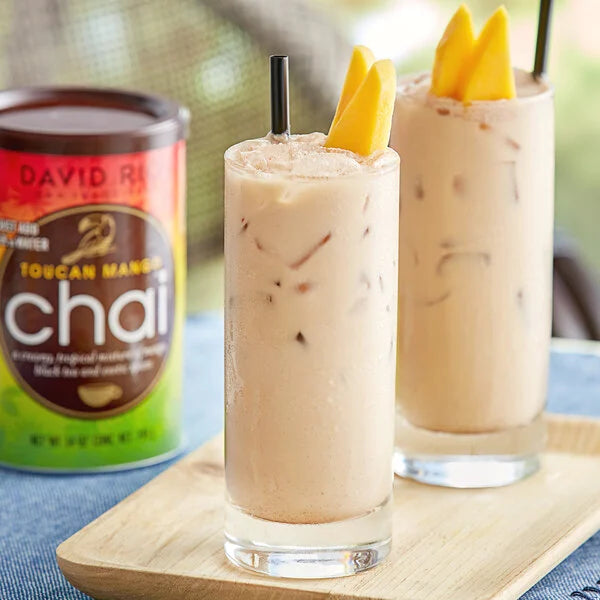 Iced latte z David Rio Toucan Mango Chai – dwa schłodzone napoje z mango na tacce, z puszką chai w tle w ujęciu lifestyle