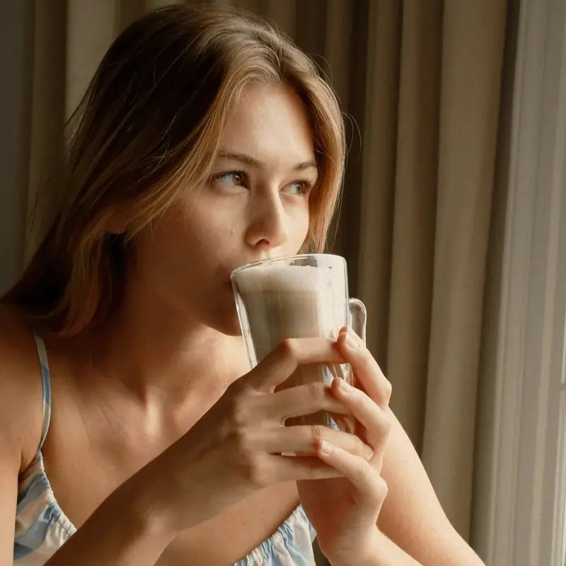 Kobieta pijąca kawę lub mleko w domu, relaksująca się przy oknie