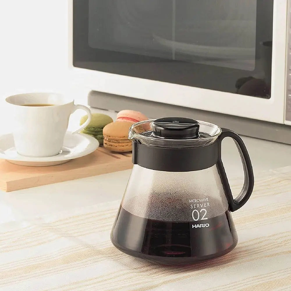 Szklany serwer do kawy Hario Range Server V60 02 z zaparzoną kawą, dzbanek ustawiony na kuchennym blacie obok filiżanki i mikrofalówki, zdjęcie lifestyle