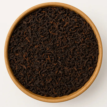 Sypane liście indyjskiej herbaty Assam Fairtrade widziane z góry na białym tle, wypełniające całą kompozycję