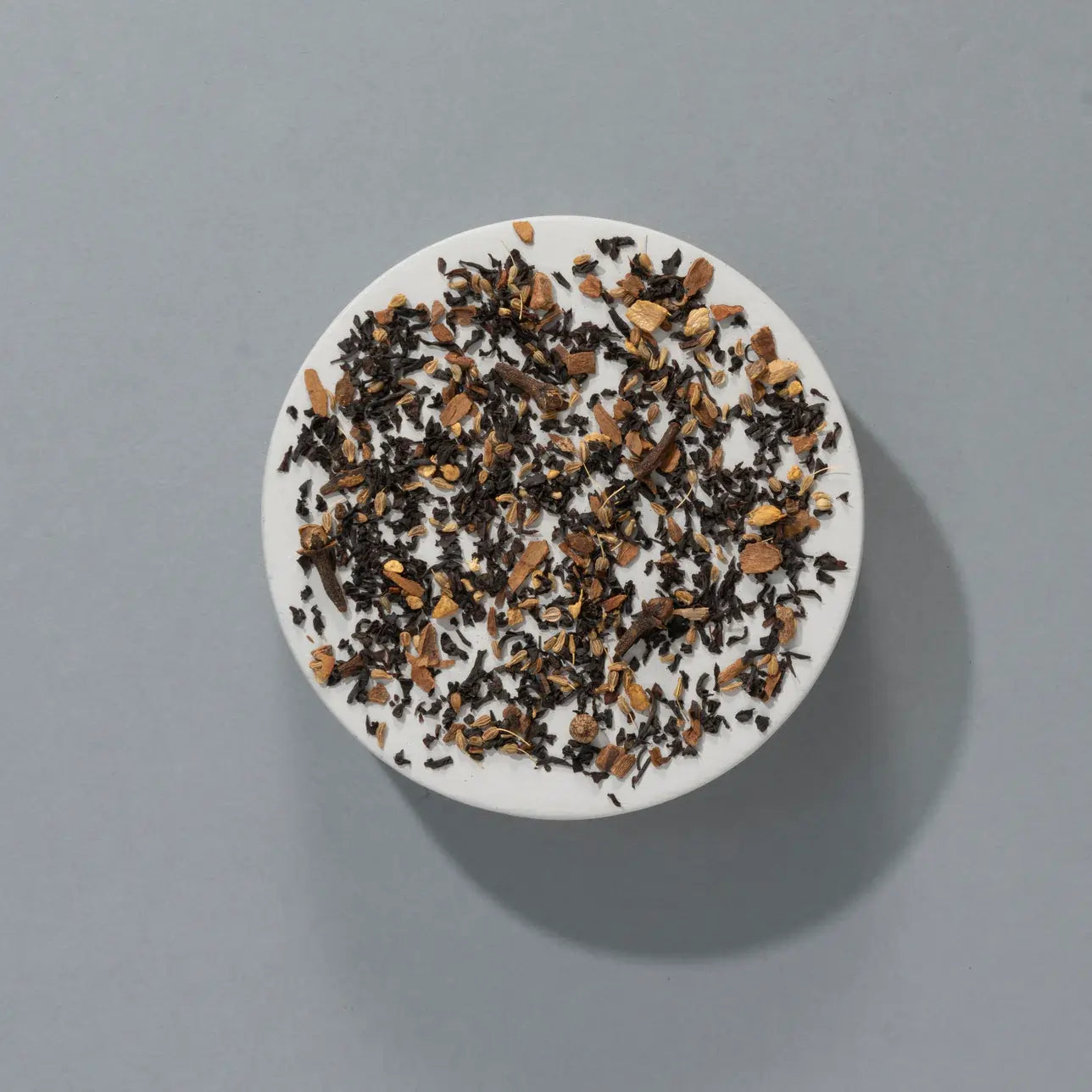 Liście czarnej herbaty Indian Spiced Chai SUKI z kawałkami imbiru i cynamonu – aromatyczna mieszanka sypana na talerzyku, widok z góry