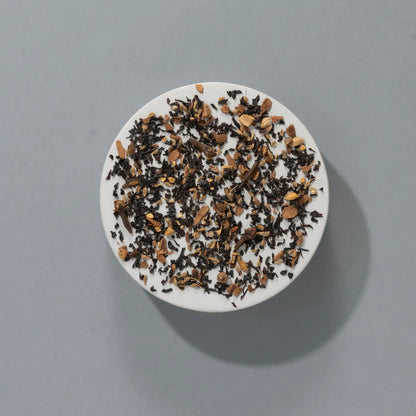 Liście czarnej herbaty Indian Spiced Chai SUKI z kawałkami imbiru i cynamonu – aromatyczna mieszanka sypana na talerzyku, widok z góry