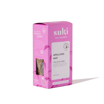 Herbata owocowa Suki Apple Loves Mint 80 g w różowym opakowaniu, widok pod kątem na pudełko z okienkiem.
