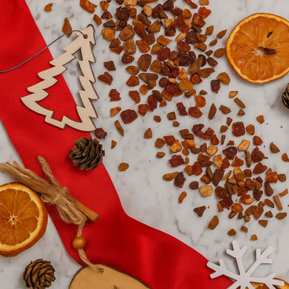 Herbata owocowa Partridge in a Pear Tea SUKI Tea – rozsypane suszone owoce i przyprawy na marmurowym tle z czerwonym materiałem, suszonymi pomarańczami, szyszkami i świątecznymi ozdobami.