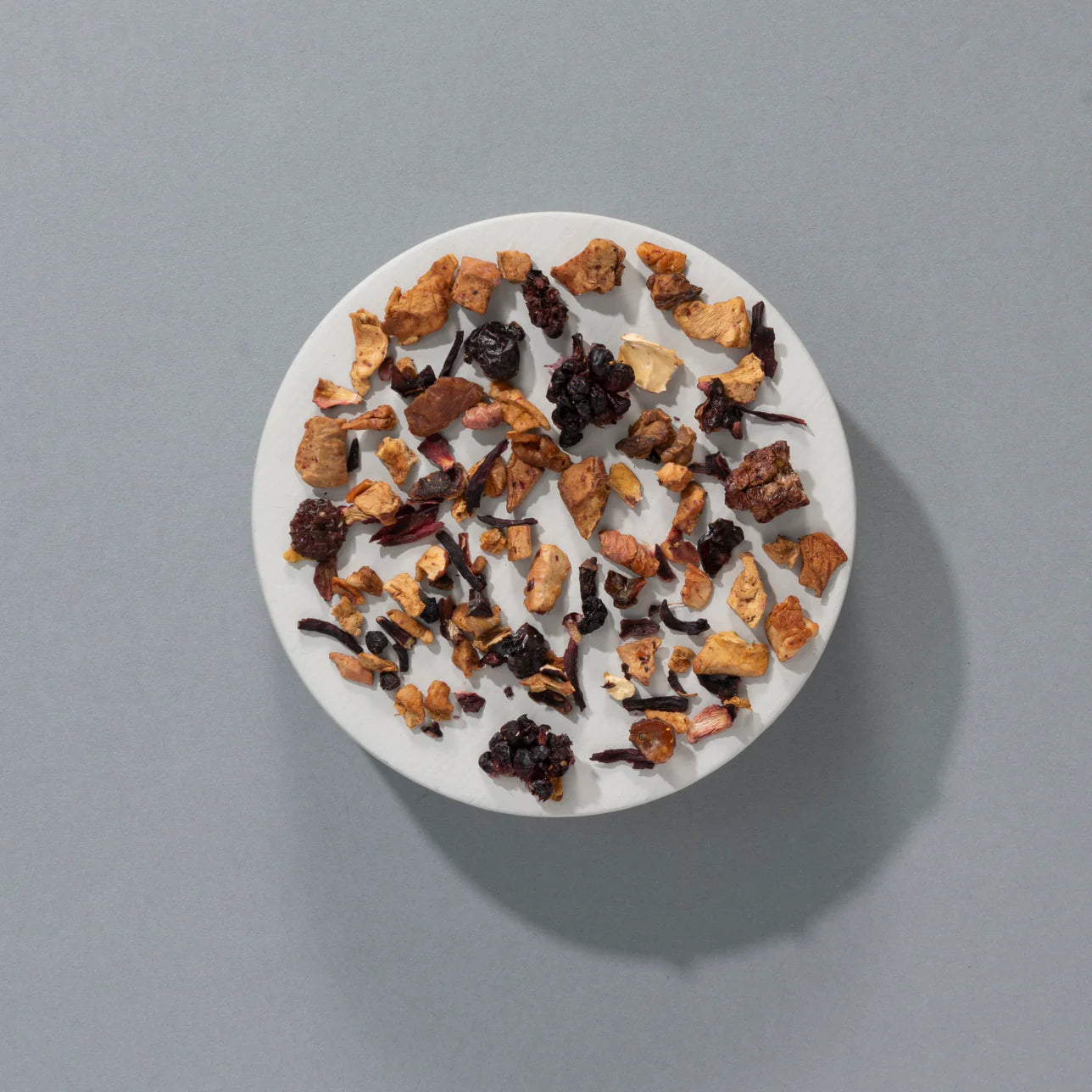 Herbata owocowa SUKI Tea Bramble Loose – kawałki jabłka, hibiskusa, jeżyn, czarnej porzeczki i malin na białym talerzyku, widok z góry.