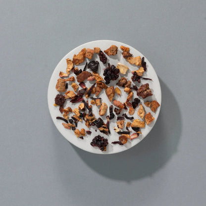 Herbata owocowa SUKI Tea Bramble Loose – kawałki jabłka, hibiskusa, jeżyn, czarnej porzeczki i malin na białym talerzyku, widok z góry.