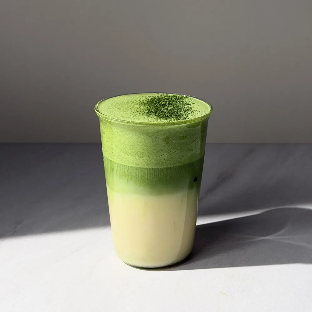 Warstwowe iced matcha latte przygotowane z PerfectTed Ceremonial Grade Matcha i napoju roślinnego Sproud Vanilla, podane w szklance z delikatną pianką i posypką z matchy.
