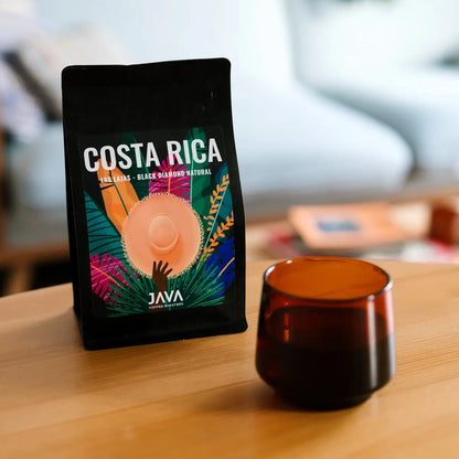Kawa specialty JAVA Coffee Costa Rica Las Lajas Black Diamond Natural w czarnym opakowaniu na stole obok bursztynowej filiżanki z kawą