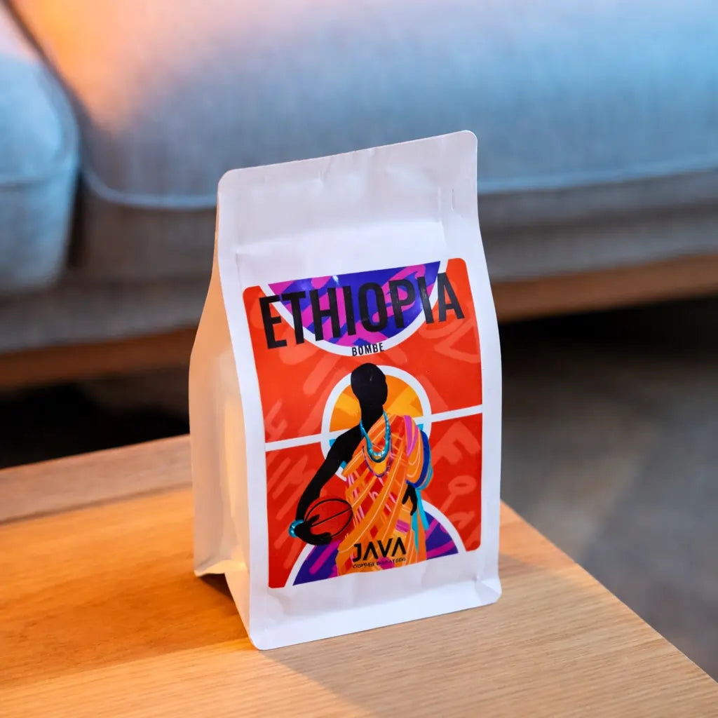 Kawa ziarnista Ethiopia Bombe JAVA Coffee Roasters – opakowanie kawy specialty na drewnianym stoliku, ujęcie lifestyle w ciepłym świetle
