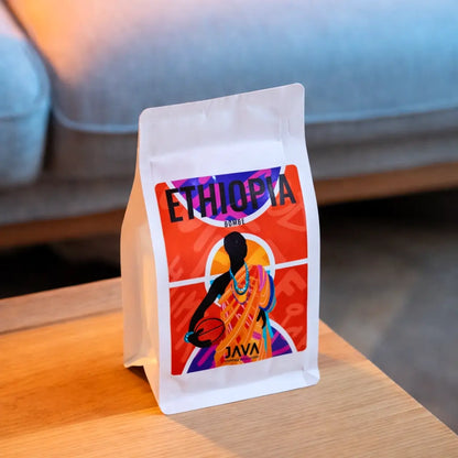 Kawa ziarnista Ethiopia Bombe JAVA Coffee Roasters – opakowanie kawy specialty na drewnianym stoliku, ujęcie lifestyle w ciepłym świetle