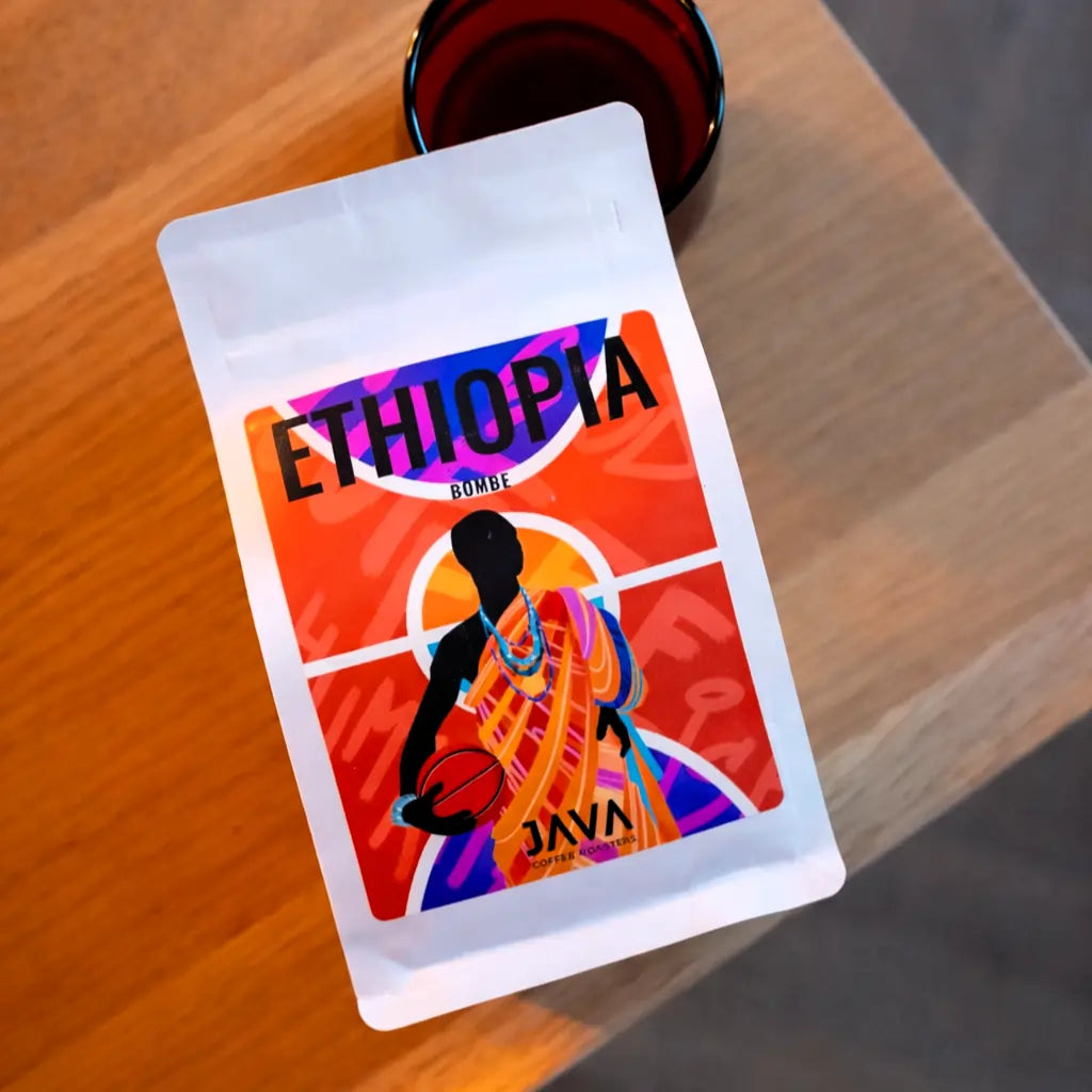 Kawa ziarnista Ethiopia Bombe JAVA Coffee Roasters – opakowanie kawy specialty na drewnianym stoliku, ujęcie lifestyle w ciepłym świetle