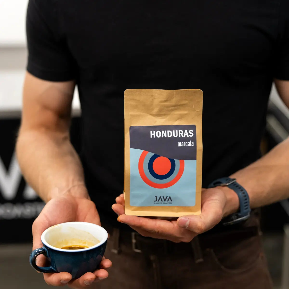 Barista trzymający opakowanie kawy specialty Honduras Marcala od JAVA Coffee Roasters oraz filiżankę świeżo zaparzonego espresso.