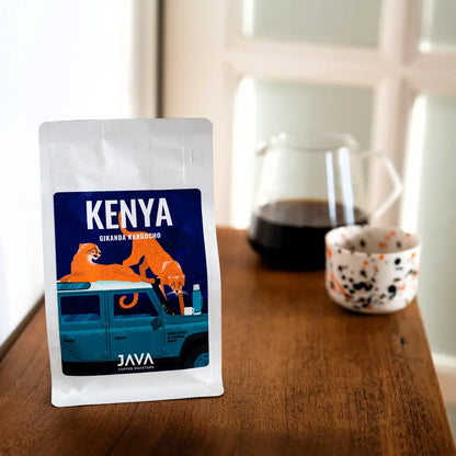 Kawa ziarnista Kenya Gikanda Kangoch od JAVA Coffee Roasters – opakowanie kawy, zaparzona kawa w szklanym dzbanku oraz filiżanka czarnej kawy na drewnianym stole, ujęcie z góry.