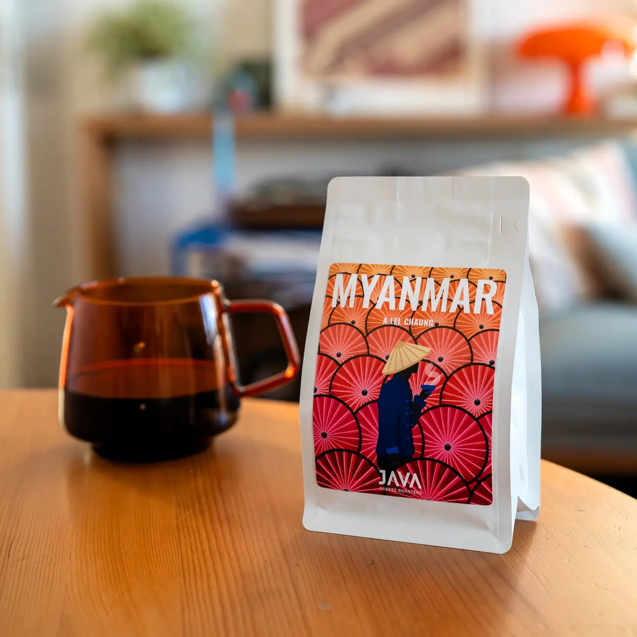 Kawa ziarnista Myanmar Ale Chaung od JAVA Coffee Roasters na drewnianym stole obok dzbanka z czarną kawą