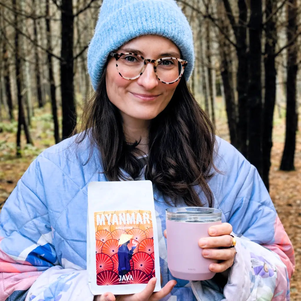 Kawa ziarnista Myanmar Ale Chaung od JAVA Coffee Roasters – kobieta w lesie trzyma opakowanie kawy i kubek z napojem
